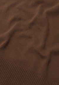 Brązowa dzianina o gładkiej fakturze i prążkowanym obszyciu. Materiał wydaje się miękki i lekki, prezentując jednolity kolor na całej powierzchni.