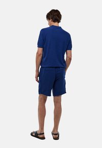 Polo bleu marine à manches courtes et coupe décontractée, accompagné d'un short bleu marine assorti. Le matériau semble texturé ; sandales incluses.