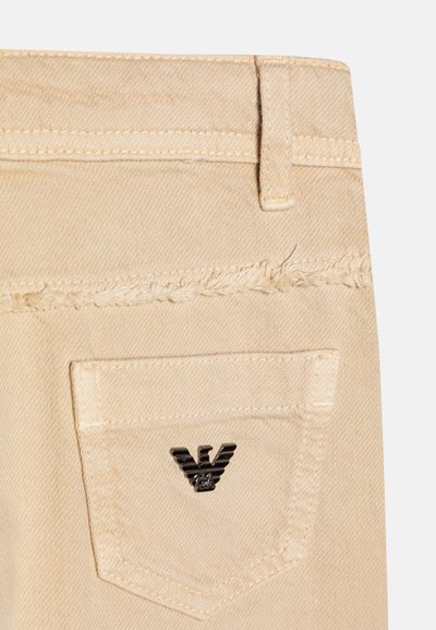 Béžové denim šortky s orezaným okrajom, so zadnou vreckom a čiernym kovovým logom. Šité detaily pozdĺž pásu.