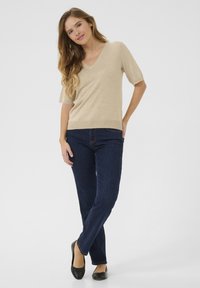 Beige V-hals sweater met korte mouwen, gecombineerd met donkerblauwe rechtvale jeans en zwarte platte schoenen. Glad textuur, casual ontwerp.