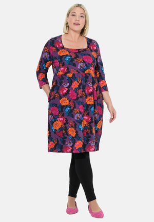 Robe fleurie violet foncé, ornée de fleurs colorées en rose, orange et bleu. Manches trois-quarts, longueur genoux, avec poches. Leggings noirs.