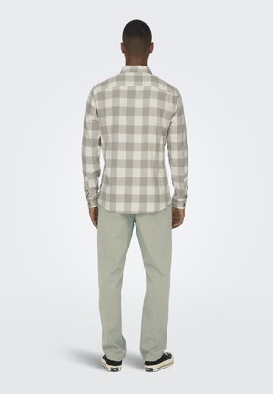 Gray and white plaid flannel shirt with long sleeves, button cuffs, and curved hem, paired with light green pants and black sneakers.
