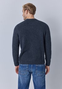 Dunkelgrauer Strickpullover mit geripptem Saum, rundem Ausschnitt und langen Ärmeln, kombiniert mit blauen Jeans mit Gesäßtaschen.