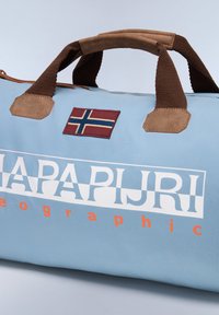 Borsa a duffel di colore blu chiaro con accenti in pelle marrone, tessuto texturizzato, manici per il trasporto e una patch con la bandiera norvegese. Grande logo bianco e testo arancione.