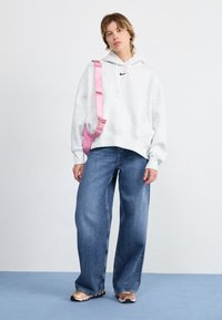 Grijze katoenen hoodie met aantrekkoord, zwart logo, gecombineerd met losse blauwe denim jeans en een roze schoudertas. Het schoeisel heeft een textuur ontwerp.