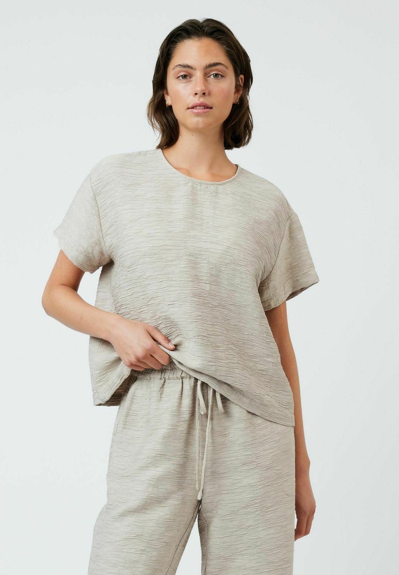 Haut texturé beige clair à manches courtes et col rond, associé à un pantalon à taille élastique assorti. Tissu doux et respirant.