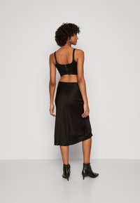 Schwarzes Satin-Zweiteiler-Outfit mit einem cropped Oberteil, das einen Reißverschluss auf dem Rücken hat, und einem knielangen Rock, kombiniert mit schwarzen Knöchelstiefeln.