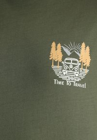 Camiseta verde oliva con un gráfico de una furgoneta vintage rodeada de árboles, montañas y sol, con el texto "Es hora de viajar" debajo.