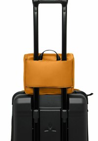 Maleta rígida negra con asa retráctil, cubierta con una bolsa de tela naranja con cremallera que cuenta con un pequeño asa de transporte.