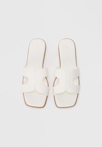 Sandale albe cu talpă plată, cu un upper sintetic neted, având două curele late și un design cu vârful pătrat. Talpă de culoare maronie deschisă. Stil minimalist.
