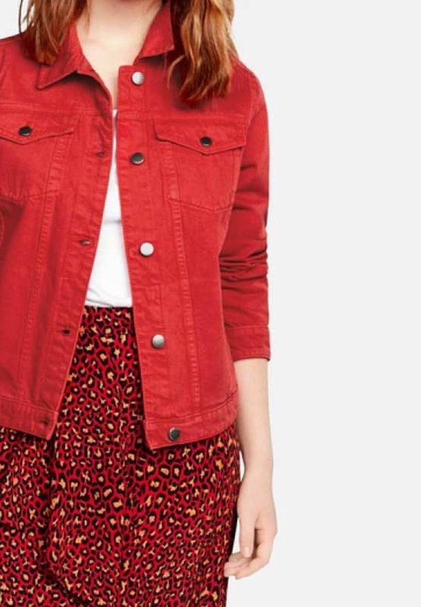 Rød denimjakke med to brystlommer, metalknaplukning og lange ærmer, parret med en mønstret rød og sort leopardprint nederdel.