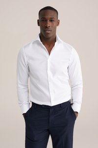 Witte overhemden met een gestructureerde kraag, lange mouwen en knopen. Gecombineerd met donkere broek met krijtstreep, met een getailleerde pasvorm.