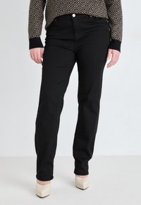 Pantalon en denim noir avec une coupe droite, doté d'une taille haute et de coutures subtiles. Associé à des chaussures à talons blocs de couleur claire.
