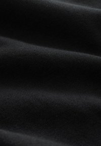 Nahaufnahme von weichem, schwarzem Stoff mit sichtbarer Textur und sanften Falten, die subtile Schatten und Tiefe erzeugen.