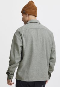 Grijze wolmix jas met een kraag, lange mouwen en knoopmanchetten, gecombineerd met een bruine geribde beanie. Heeft een soepele textuur en een ontspannen pasvorm.