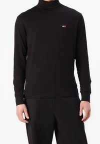 Black long-sleeve turtleneck shirt made of soft fabric, featuring a small logo on the chest and fitted cuffs.