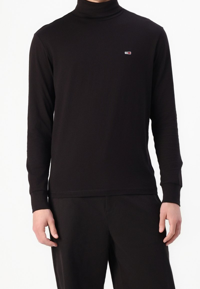 Black long-sleeve turtleneck shirt made of soft fabric, featuring a small logo on the chest and fitted cuffs.