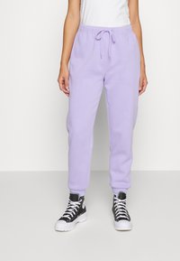 Lilac sweatpants made of soft cotton blend, featuring an elastic waistband with drawstring, tapered cuffs, and side pockets. Worn with black sneakers.