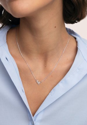 Collar de plata de ley con una cadena delicada y un colgante en forma de estrella con pequeñas piedras preciosas, llevado sobre una camisa azul clara.