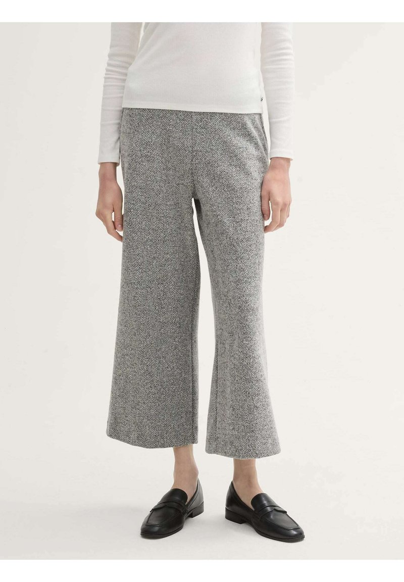 Grijze broek met een visgraatpatroon en wijde pijpen, gemaakt van textuurstof, gecombineerd met zwarte instappers. De tailleband is elastisch voor extra comfort.