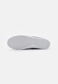 Witte sneakerzool met een gestructureerd grijs rubberoppervlak, voorzien van een geometrisch patroon en het reliëflogo "TOMMY HILFIGER" op het hielgedeelte.