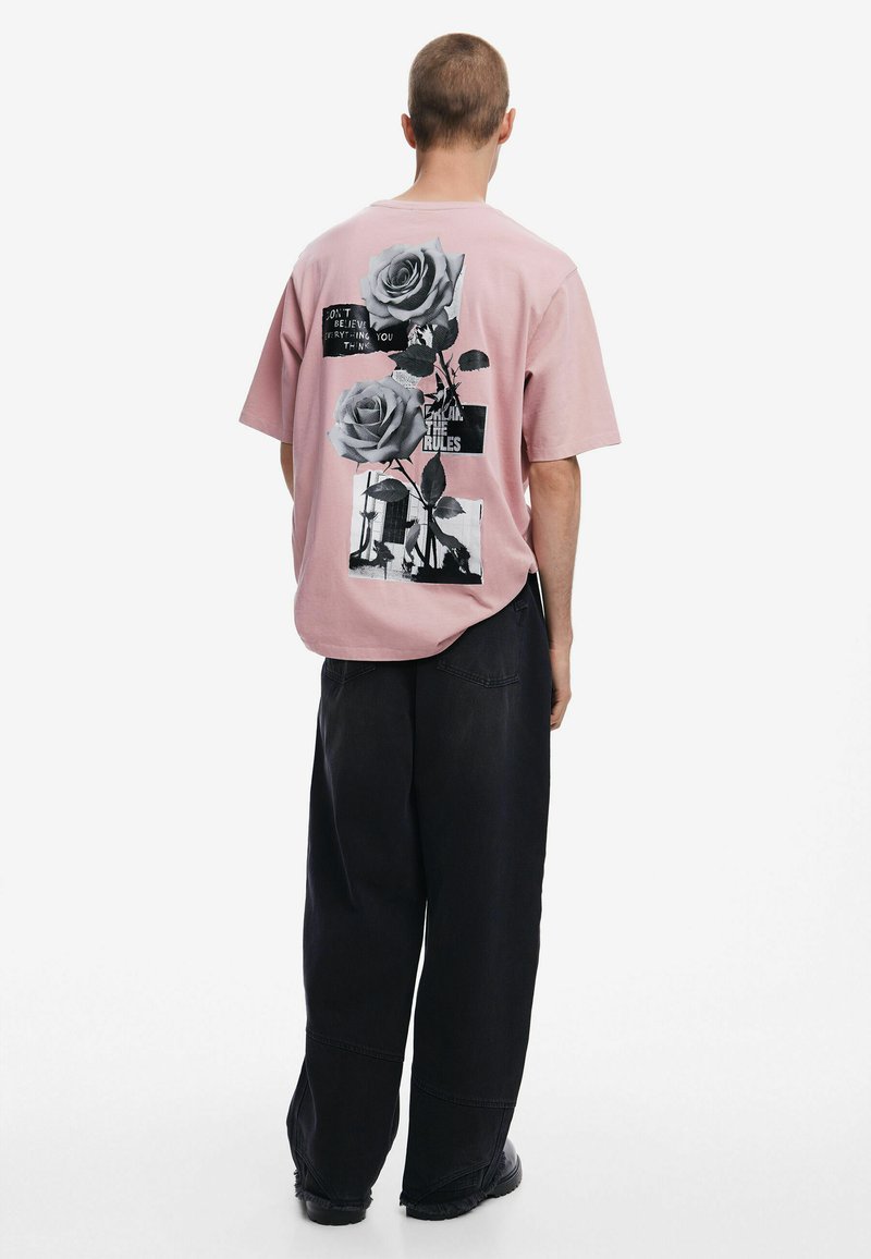 Pink short-sleeve shirt with black graphic prints featuring roses and text on the back. Loose fit with a round neckline and relaxed design.