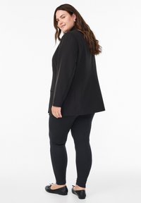 Americana negra con un diseño estructurado, llevada sobre leggins negros ajustados, combinada con bailarinas negras. Tela suave y ajuste a medida.