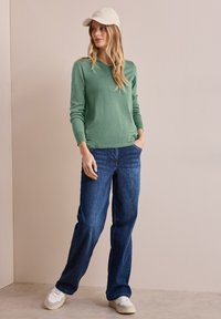 Minzgrüner Strickpullover mit Rundhalsausschnitt, kombiniert mit lässigen blauen Jeans und weißen Sneakers. Warmer, weicher Stoff.