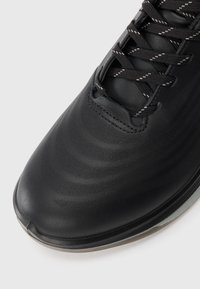 Close-up of a black sneaker toe with textured synthetic upper and black laces featuring white reflective details on a white background.