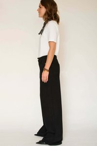 Pantalon large noir taille haute, associé à une chemise blanche à manches courtes et une écharpe noire à motifs, porté avec des chaussures noires à bout pointu.