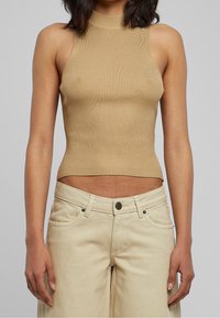 Opalony prążkowany top bez rękawów z wysokim kołnierzem, dopasowany fason, krótka długość, zestawiony z jasnymi, szerokimi dżinsami.