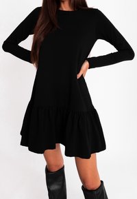 Czarna sukienka z długim rękawem i rozkloszowanym dołem, wykonana z miękkiego materiału, z okrąg�łym dekoltem i luźnym krojem. Para czarnych kozaków za kolano.
