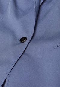 Ljusblått tyg med en slät yta, med en svart knapp och en subtil diagonalt vävda mönster. Kantsynligt skräddarsytt krage.