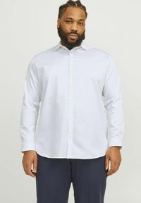 White long-sleeve button-up shirt with a collared neck, featuring a smooth texture and standard fit, paired with navy trousers.