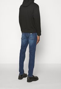 Svart hoodie med avslappnad passform, kombinerad med blå denimjeans. Jeans har sömldetaljer och en lätt blekt yta. Svarta skor.