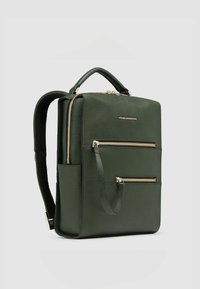 Mochila de cuero verde con dos bolsillos frontales con cremallera, un asa superior y correas ajustables. Presenta detalles en hardware dorado y superficie texturizada.