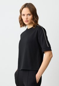 Czarna koszulka z krótkim rękawem i okrągłym dekoltem, z metalicznym srebrnym wykończeniem na rękawach. Gładki materiał i prosty krój.