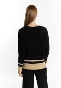 Maglione nero in lavorazione a maglia con collo tondo e maniche lunghe, caratterizzato da un orlo e polsini a righe beige. Il materiale ha una superficie morbida e liscia.