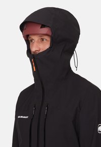 Black waterproof jacket with a high collar, adjustable hood, and orange zipper pull. Features logo and two front zippered pockets.