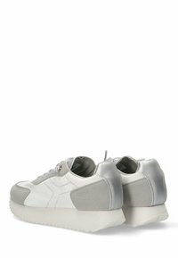 Zapatillas con una mezcla de cuero blanco y gamuza gris. Presentan un acento metálico plateado en el talón y una suela blanca gruesa. Diseño con cordones, superficies texturizadas.