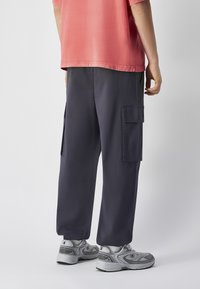 Navy cargobroek met zijzakken, gecombineerd met een koraalkleurig shirt en grijze sneakers. Een soepele stof, relaxte pasvorm en een verstelbare tailleband.