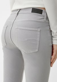 Jeans grises con un diseño ajustado, tejido texturizado y dos bolsillos traseros con detalles de costura sutiles y una etiqueta de cuero negra en la cinturilla.
