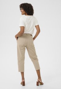 Beige, verkürzte Hosen aus Baumwolle mit einer taillierten Taille und Gesäßtaschen; kombiniert mit einem weißen kurzärmeligen Hemd und beigen Blockabsatzsandalen.
