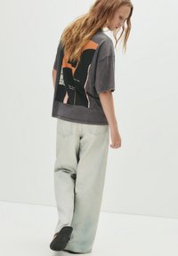Grå oversized t-shirt med grafisk print i sort, orange og pink, parret med lysvaskede bredbenede jeans og sorte slip-on sko.