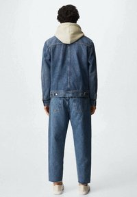 Blauwe denimjas met capuchon, gecombineerd met losse blauwe denimjeans. Opmerkelijke details zijn de zachte capuchon en gestikte accenten.