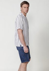 Rövid ujjú, galléros fehér ing függőleges fekete csíkokkal, sötétkék farmer rövidnadrággal, oldalsó zsebekkel párosítva.
