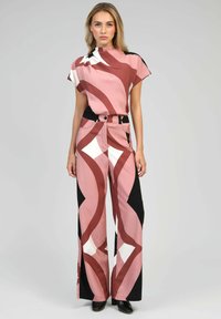 Vêtement à motifs roses et noirs comprenant un haut à col montant à manches courtes et un pantalon large, rehaussé de formes blanches audacieuses.