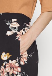 Calças florais pretas com uma textura suave, apresentando um padrão floral em rosa e amarelo, destacando um bolso lateral e uma cintura elástica.