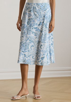 Jupe mi-longue avec motif floral cachemire bleu et blanc portée avec des sandales blanches à lanières et talon bas sur un sol en bois.