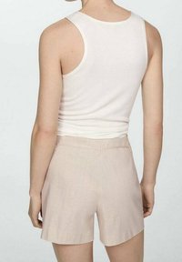 Biały top na ramiączkach i beżowe szorty wykonane z lekkiego materiału. Szorty mają luźny krój, gładką fakturę i minimalne przeszycia.